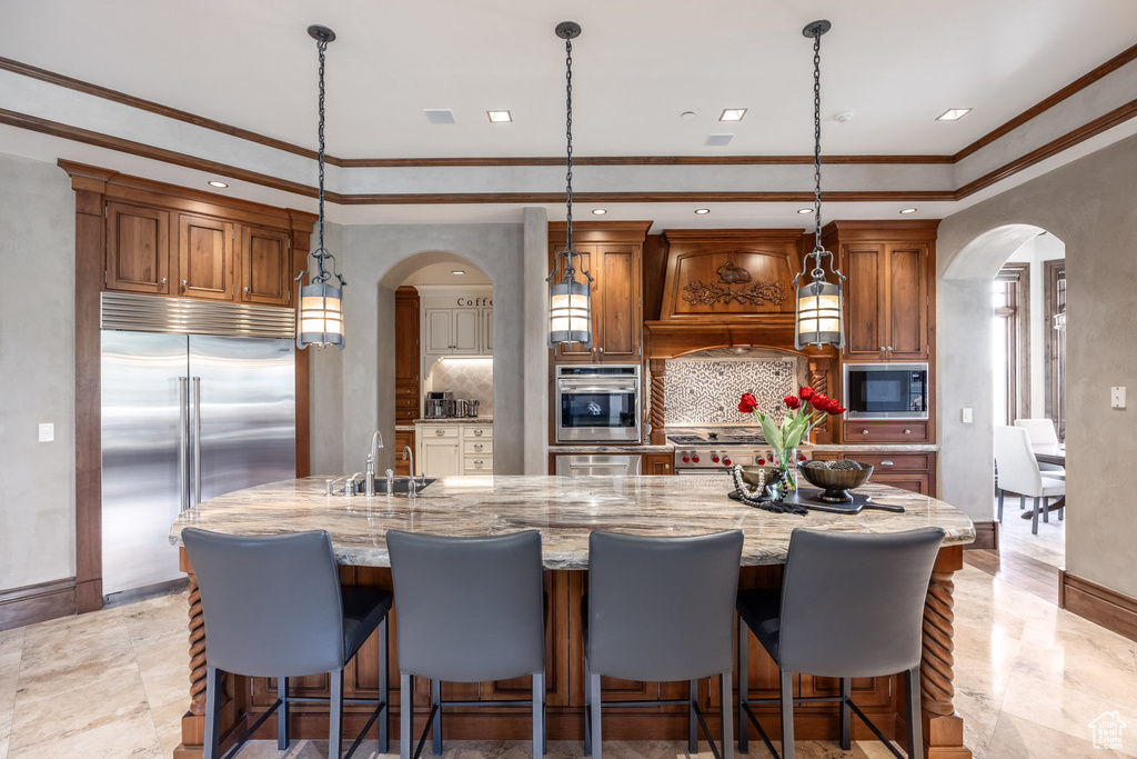 Kitchen featuring arched walkways, built in appliances, custom range hood, backsplash, and crown molding