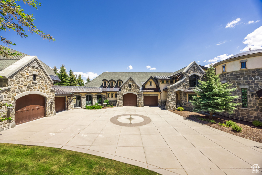View of front of home featuring stone siding, an attached garage, curved driveway, a standing seam roof, and stucco siding