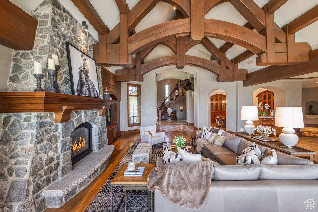 Living room with beam ceiling, arched walkways, wood finished floors, a fireplace, and high vaulted ceiling