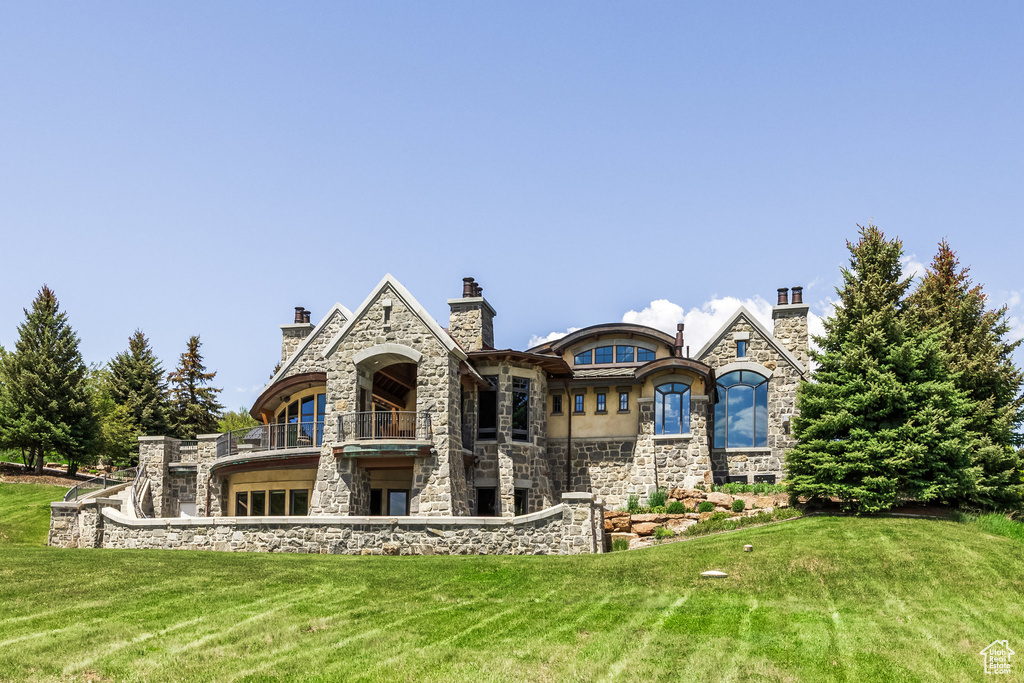 Rear view of house featuring stone siding, a lawn, and a balcony