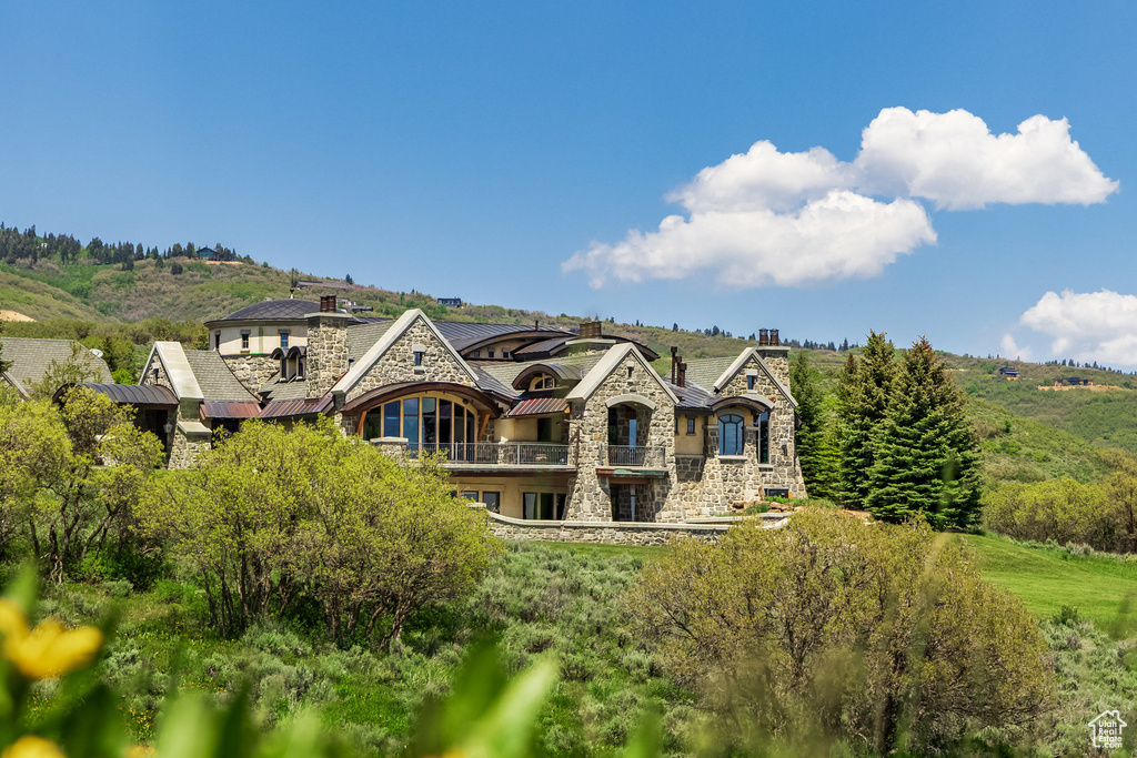 Back of house featuring stone siding, a balcony, stucco siding, and a chimney