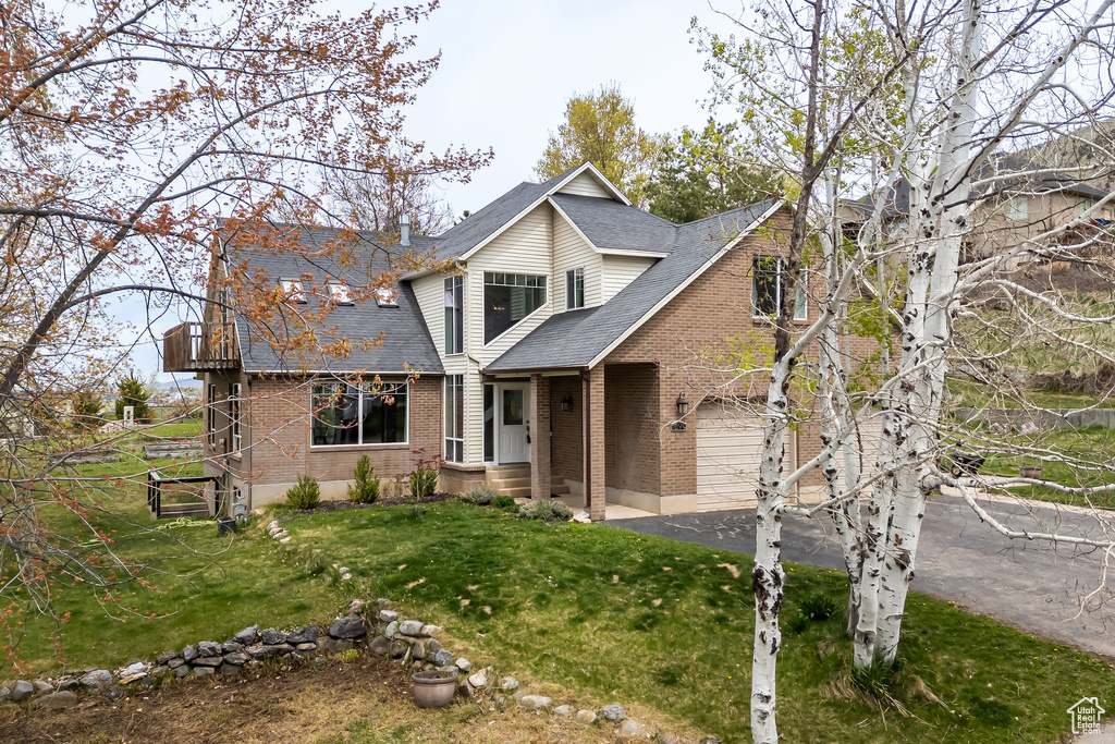 Traditional-style house featuring brick siding, roof with shingles, a front lawn, and driveway