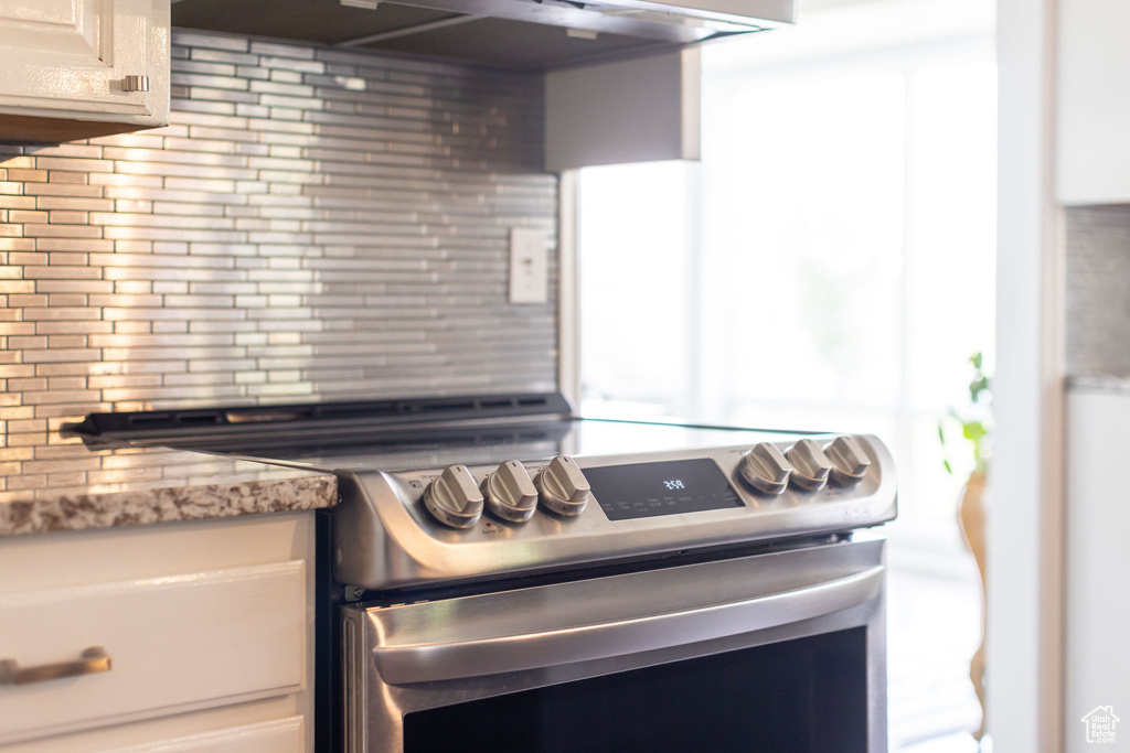 Kitchen view of stainless steel range with electric stovetop, decorative backsplash, light stone countertops, and exhaust hood