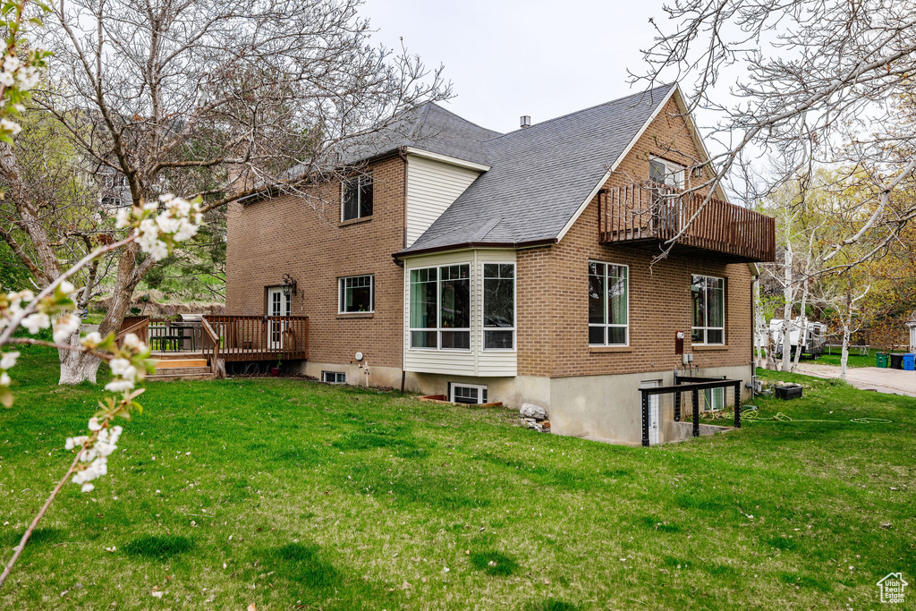 Rear view of property featuring a balcony, brick siding, a yard, a shingled roof, and a wooden deck