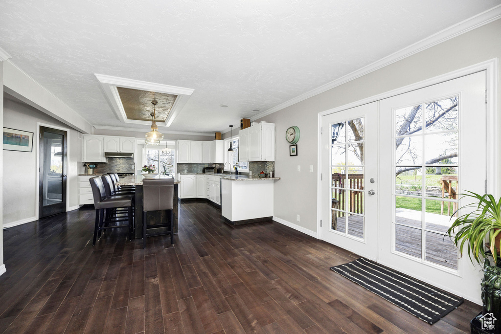 Kitchen featuring white cabinetry, decorative backsplash, a kitchen island, dark wood finished floors, and ornamental molding