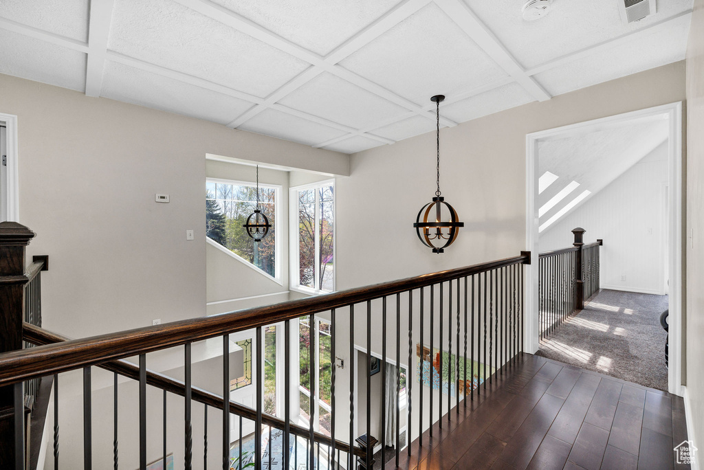 Hall featuring coffered ceiling, wood finished floors, a chandelier, beamed ceiling, and an upstairs landing