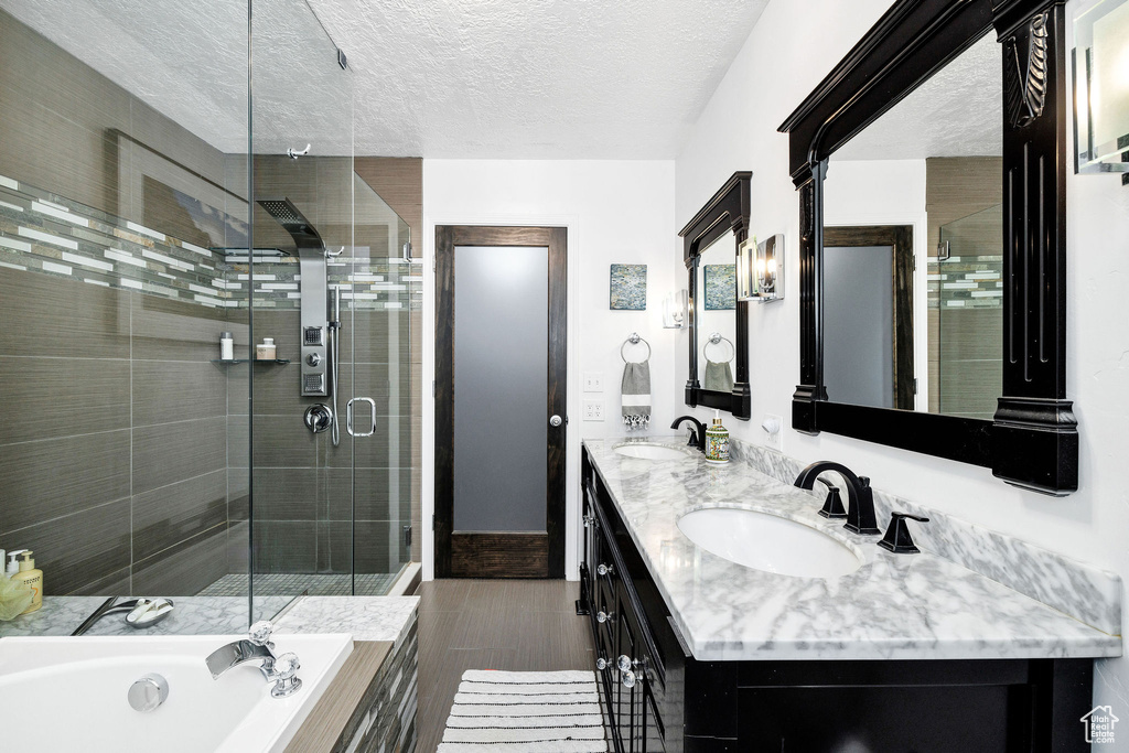Bathroom featuring a shower stall, double vanity, a garden tub, a textured ceiling, and wood finished floors