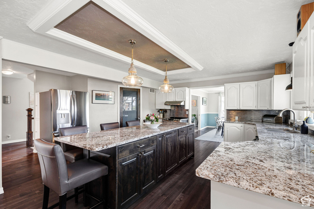 Kitchen with stainless steel fridge with ice dispenser, a raised ceiling, white cabinetry, a kitchen island, and dark wood-style floors