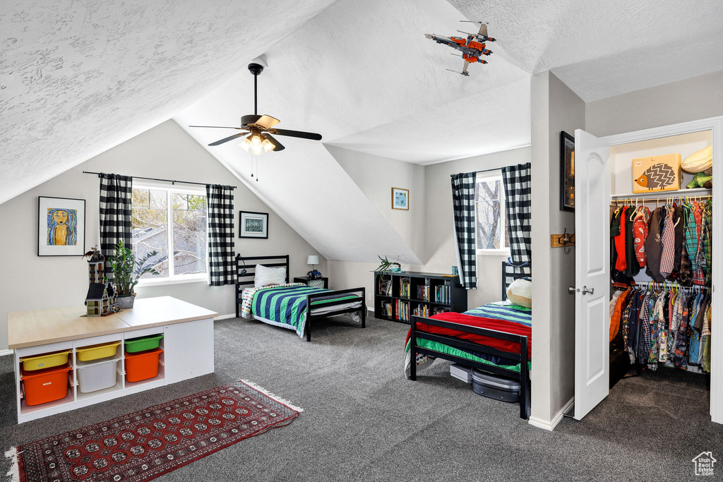 Carpeted bedroom featuring a textured ceiling, vaulted ceiling, a ceiling fan, and a walk in closet