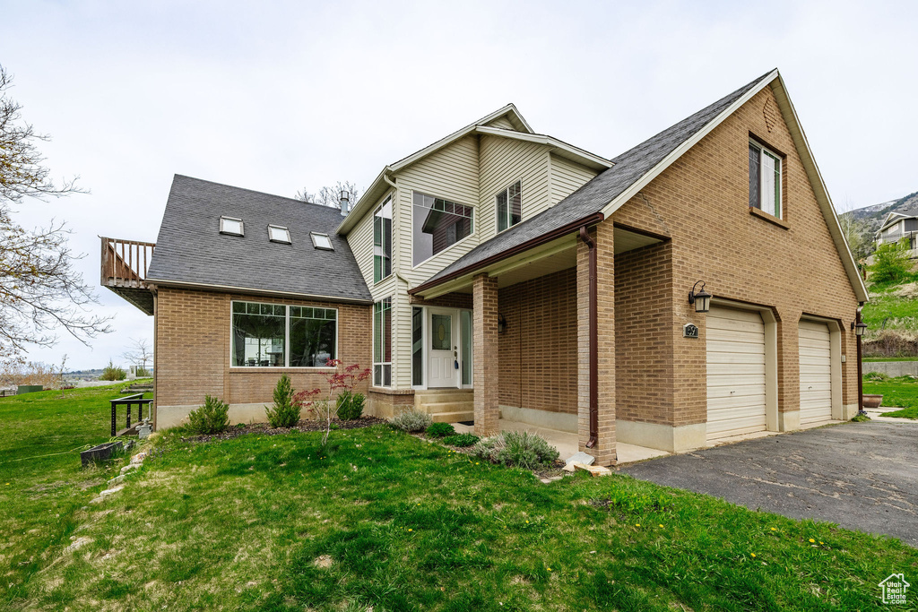 View of front of house with brick siding, a front lawn, asphalt driveway, a garage, and roof with shingles