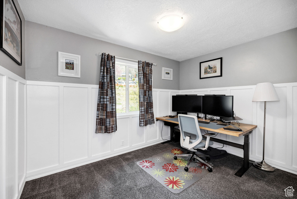 Office space featuring a textured ceiling, a decorative wall, dark carpet, and a wainscoted wall