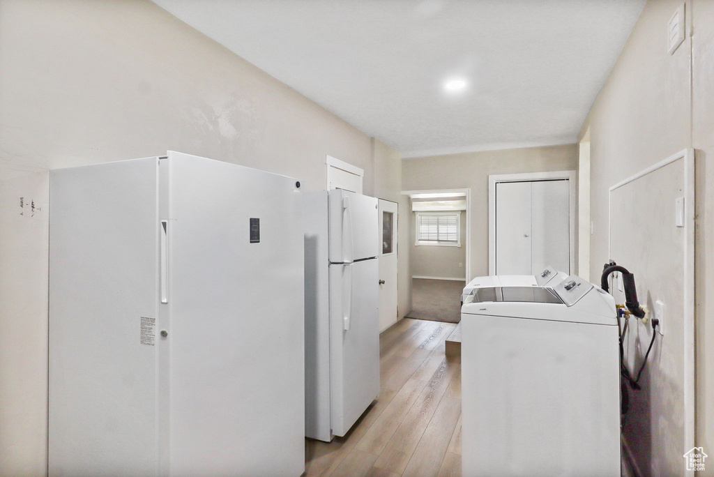 Kitchen with freestanding refrigerator, washing machine and dryer, light wood finished floors, and fridge