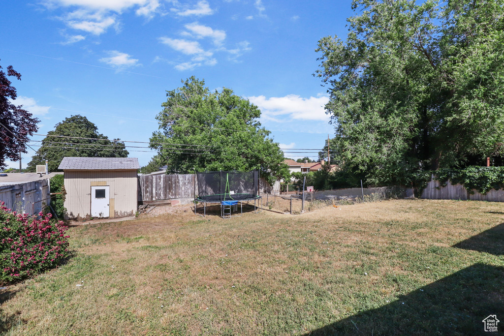 Fenced backyard featuring a trampoline and a storage shed