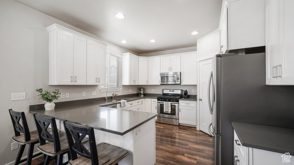 Kitchen featuring appliances with stainless steel finishes, dark countertops, a peninsula, dark wood-type flooring, and white cabinetry