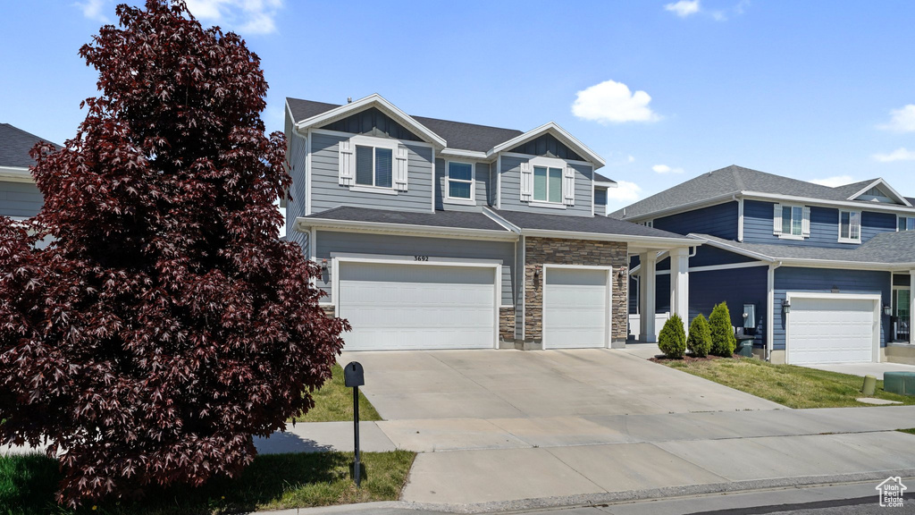 View of front of property with concrete driveway, an attached garage, stone siding, and board and batten siding