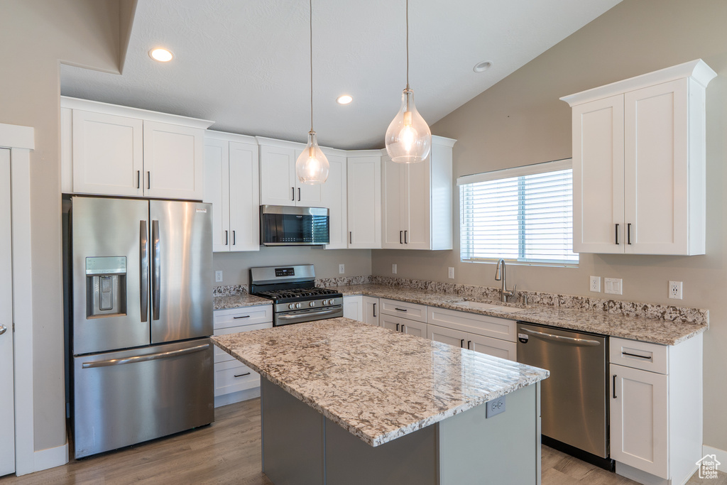 Kitchen featuring appliances with stainless steel finishes, white cabinets, lofted ceiling, a center island, and light stone countertops
