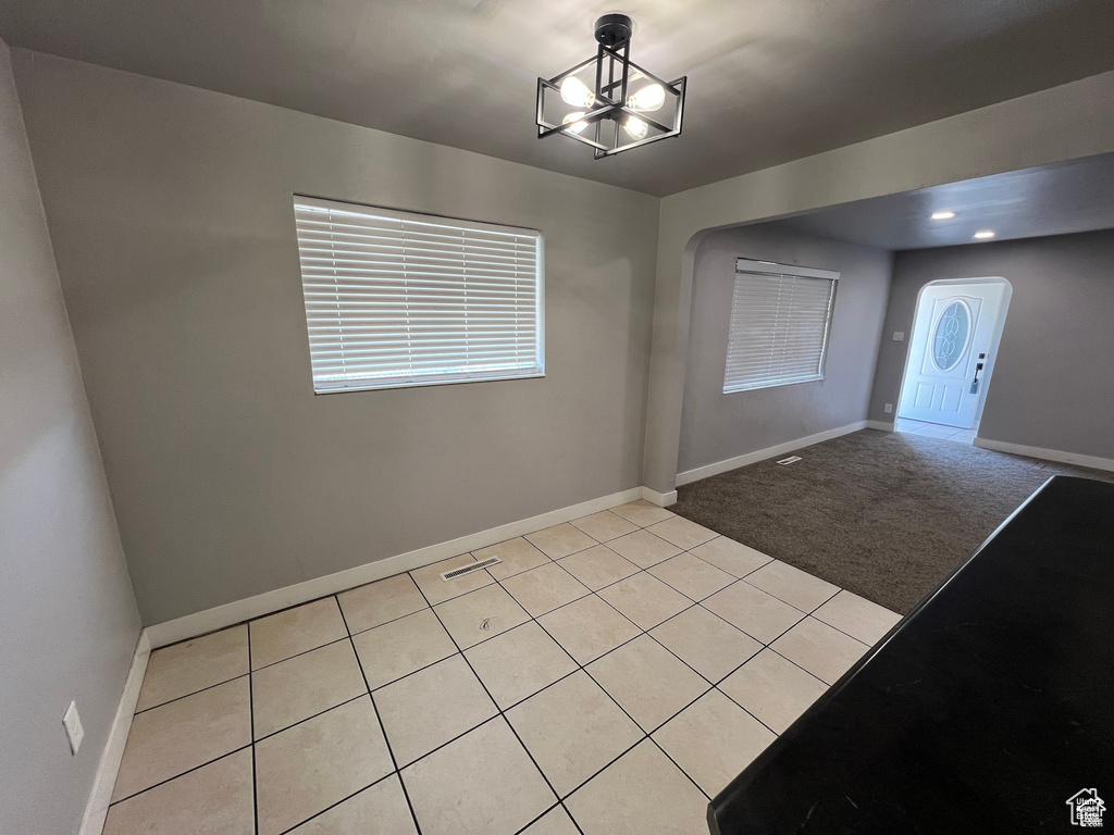 Entrance foyer featuring light tile patterned floors, arched walkways, light colored carpet, and a chandelier