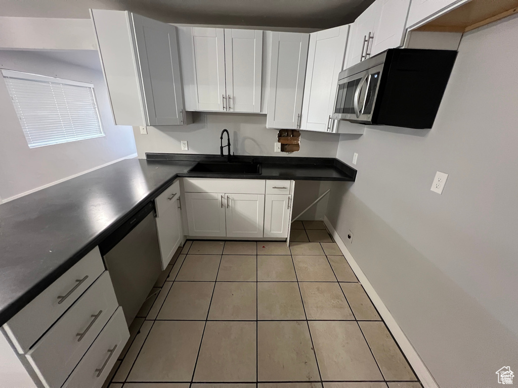 Kitchen with appliances with stainless steel finishes, dark countertops, light tile patterned flooring, and white cabinetry
