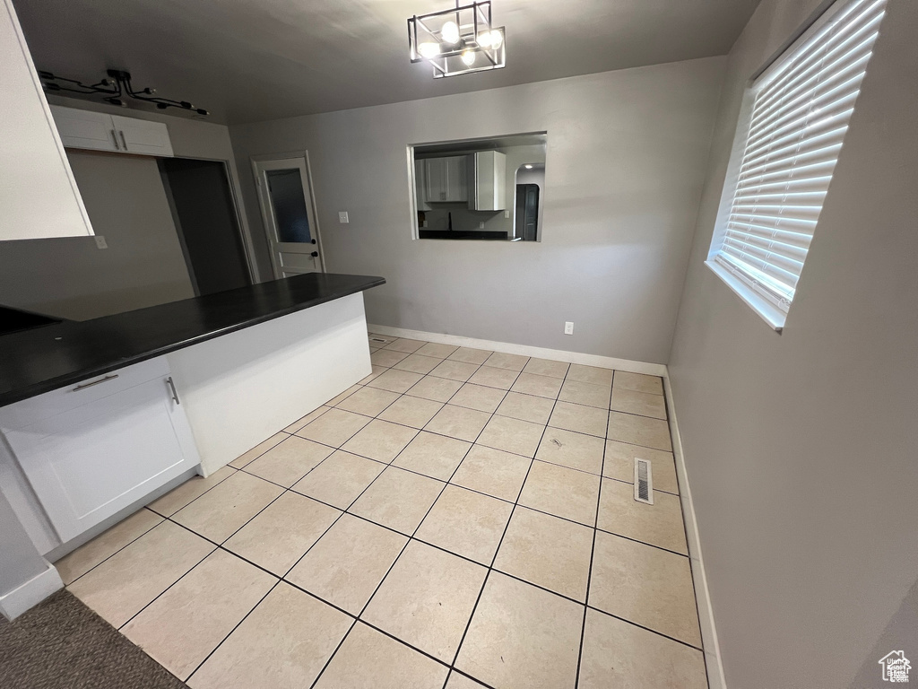 Kitchen featuring light tile patterned floors, dark countertops, white cabinets, and decorative light fixtures