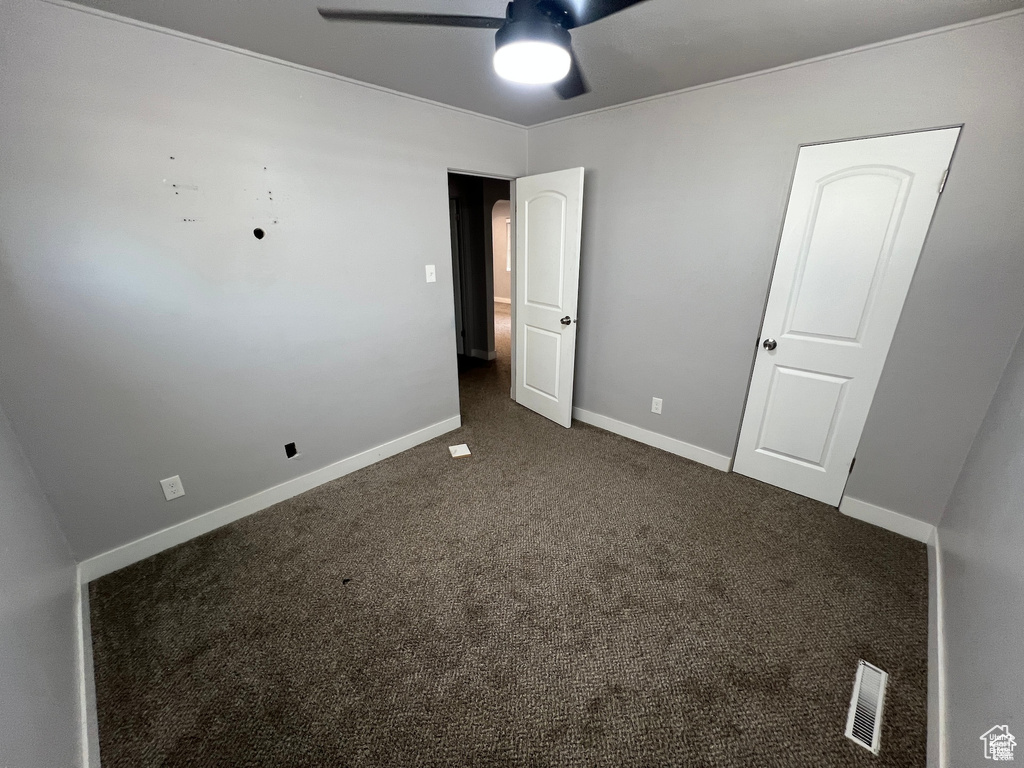 Unfurnished bedroom with dark colored carpet and a ceiling fan