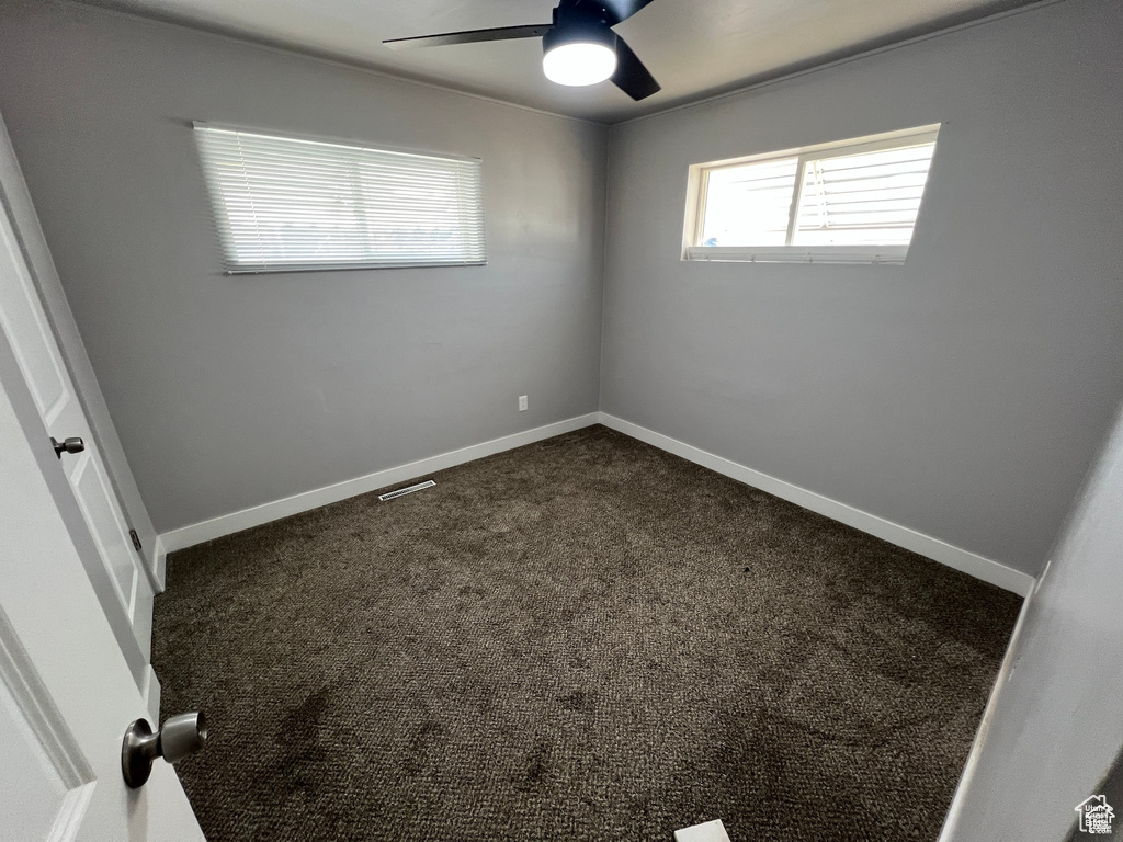 Unfurnished room with ceiling fan and dark colored carpet