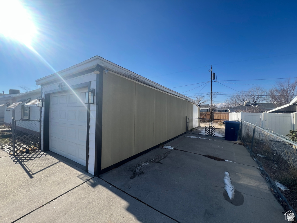 View of side of property with a detached garage, a gate, concrete driveway, and an outdoor structure