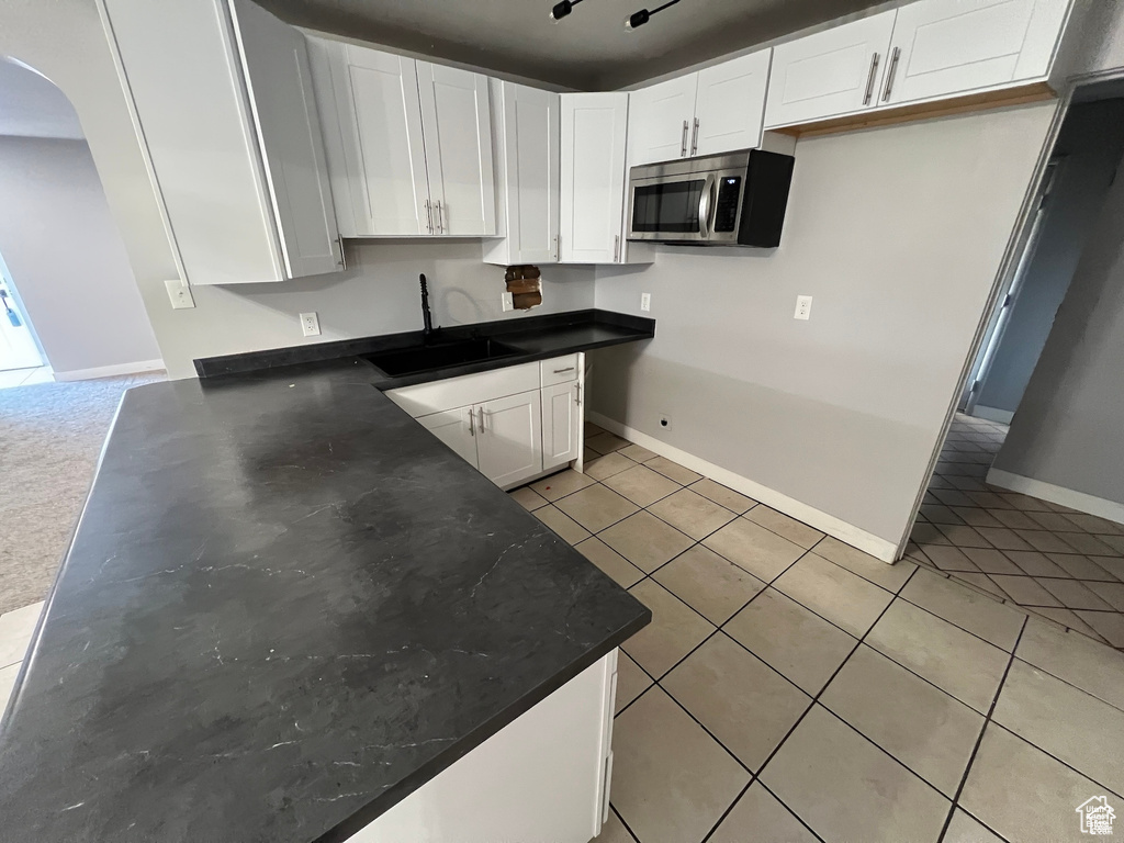 Kitchen with stainless steel microwave, light tile patterned floors, arched walkways, white cabinets, and dark countertops