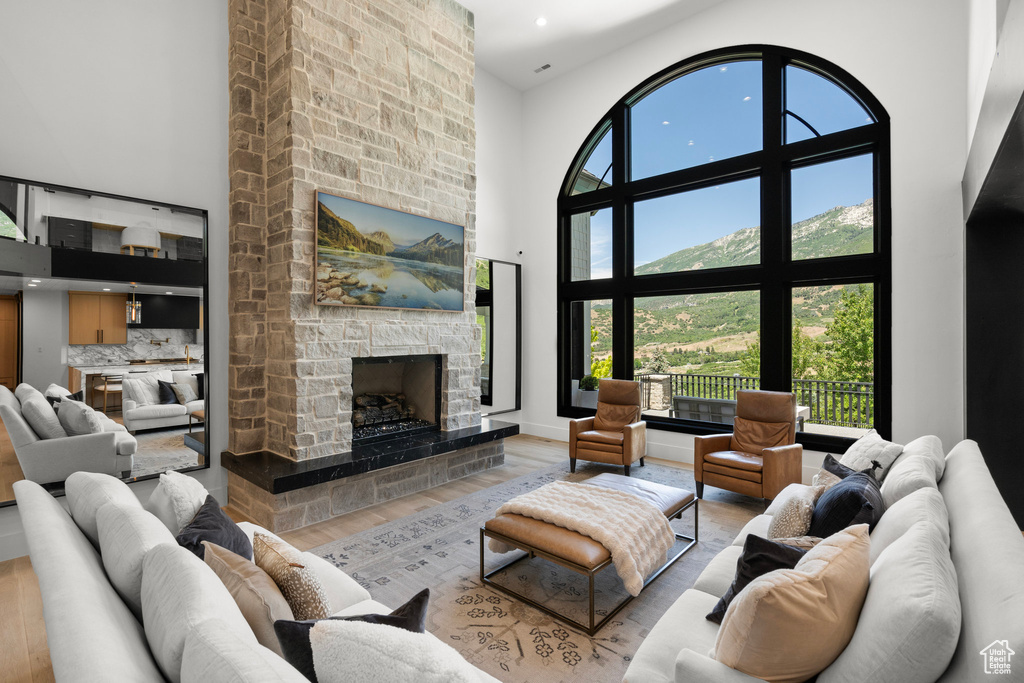 Living room with a towering ceiling, wood finished floors, a stone fireplace, healthy amount of natural light, and recessed lighting