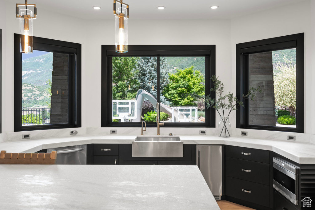 Kitchen with stainless steel appliances, dark cabinetry, recessed lighting, light stone counters, and pendant lighting