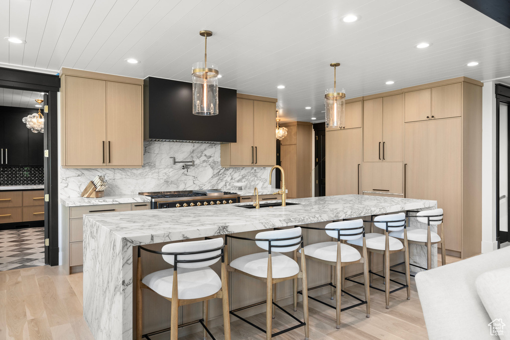 Kitchen with exhaust hood, light wood-type flooring, light brown cabinets, light stone counters, and recessed lighting