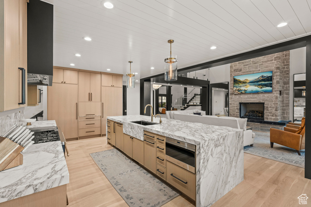 Kitchen with light brown cabinetry, light wood-style flooring, a large island with sink, light stone countertops, and recessed lighting