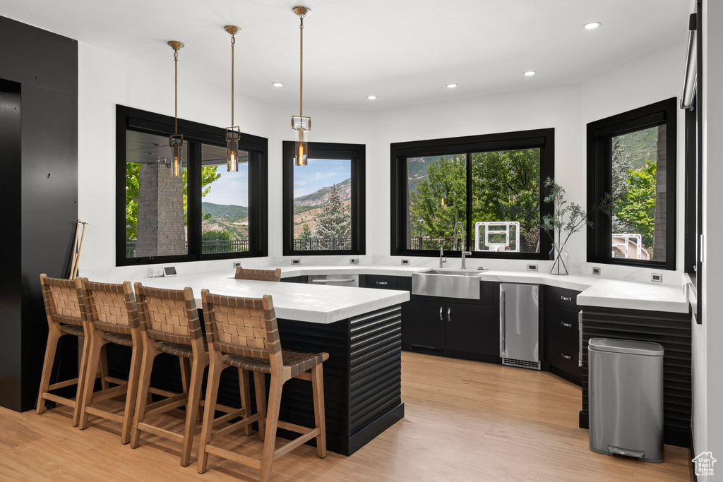 Kitchen featuring dark cabinets, light countertops, a breakfast bar, light wood finished floors, and a peninsula