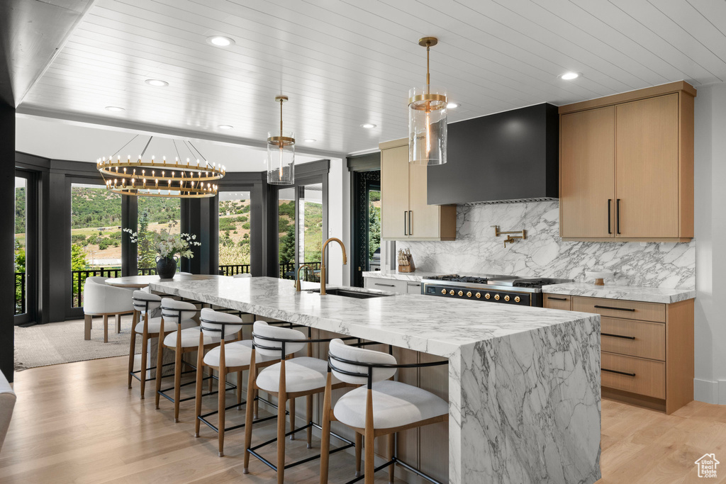 Kitchen featuring wall chimney exhaust hood, a chandelier, a large island, tasteful backsplash, and light wood finished floors