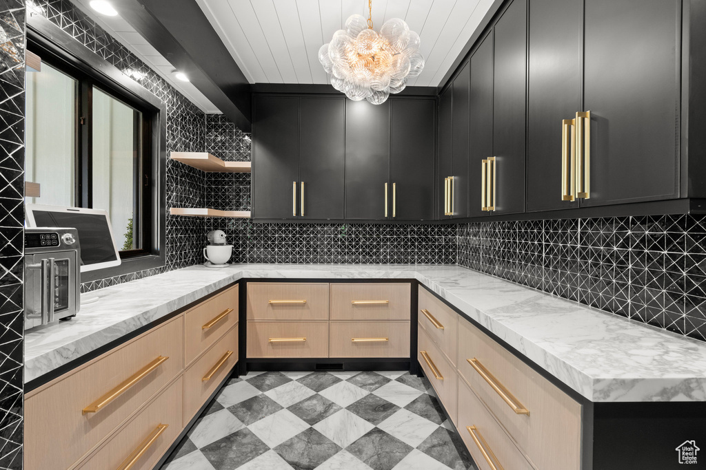 Kitchen featuring open shelves, dark cabinetry, decorative backsplash, and light stone counters