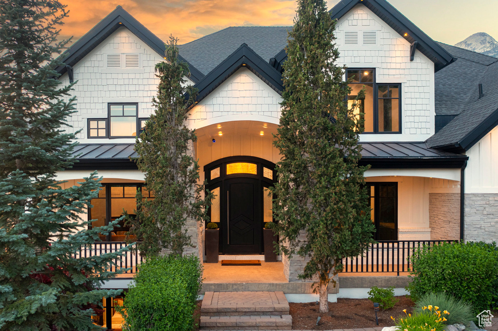 View of front of house featuring a standing seam roof, a shingled roof, covered porch, a metal roof, and stone siding