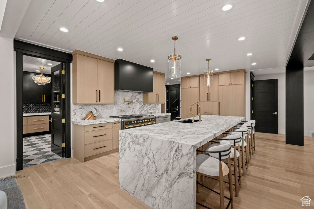 Kitchen featuring wall chimney range hood, light brown cabinets, light wood-style floors, tasteful backsplash, and recessed lighting