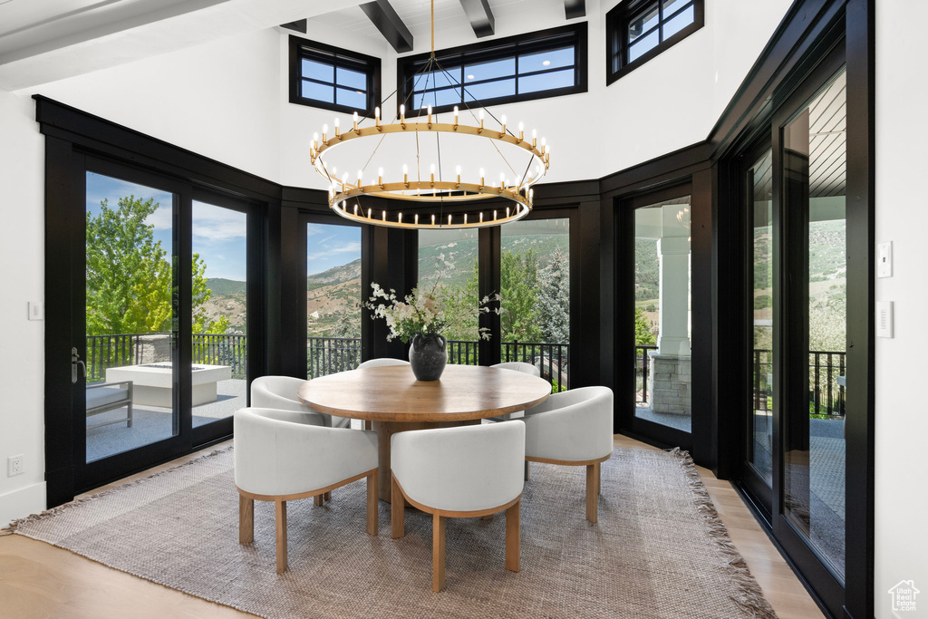 Dining room with french doors, a towering ceiling, wood finished floors, a chandelier, and beamed ceiling
