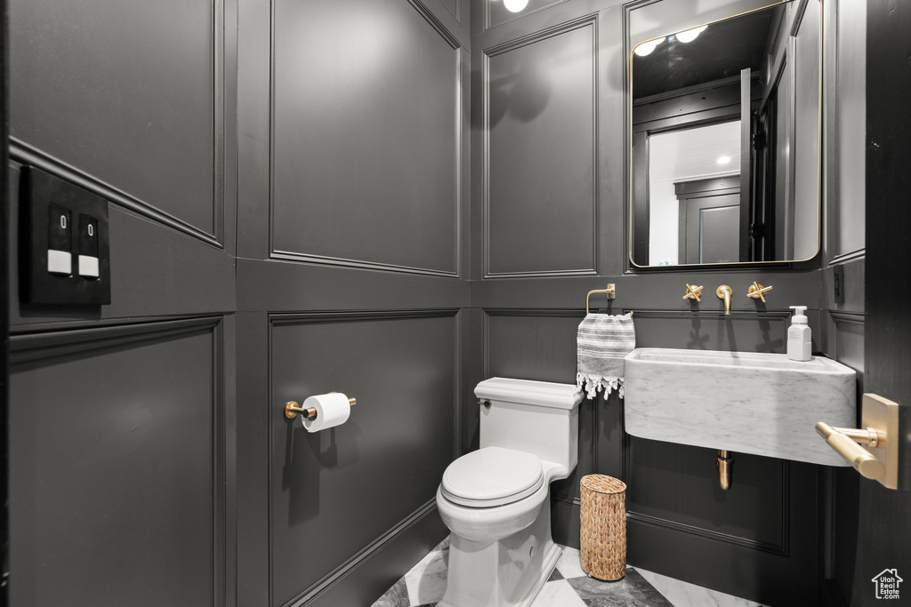 Half bathroom featuring marble look tiles and toilet