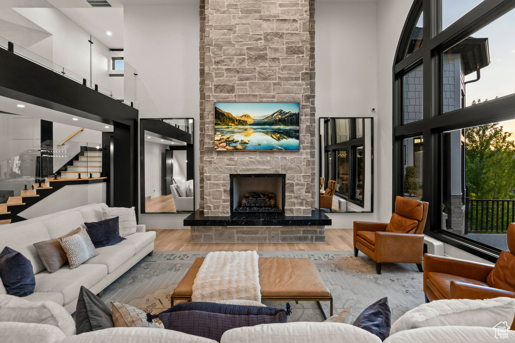 Living room featuring a high ceiling, a stone fireplace, wood finished floors, and stairs