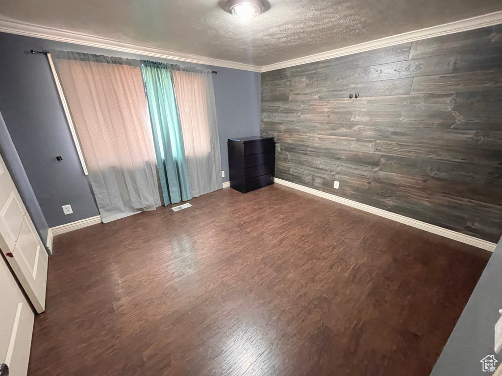 Spare room featuring wooden walls, wood finished floors, crown molding, and a textured ceiling