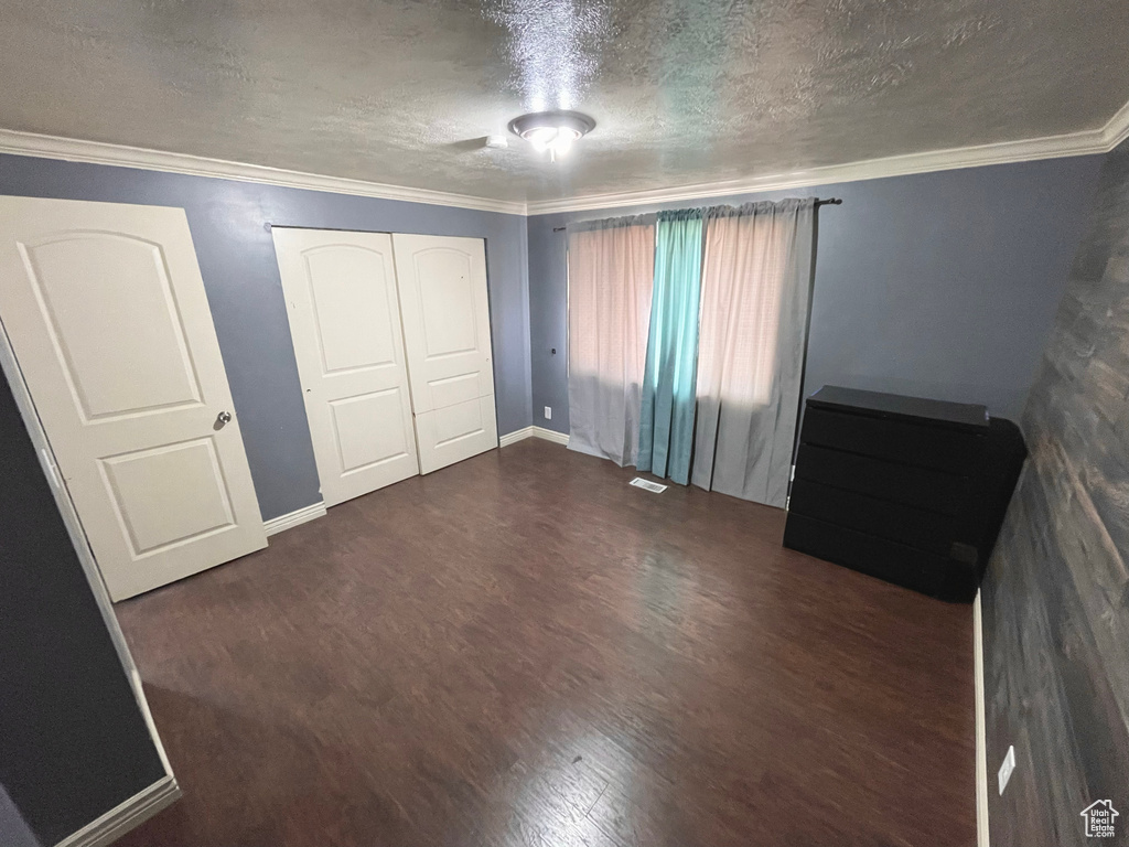 Unfurnished bedroom with wood finished floors, a textured ceiling, crown molding, and a closet