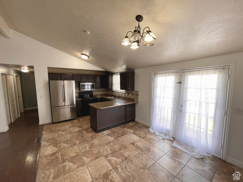 Kitchen featuring appliances with stainless steel finishes, vaulted ceiling, a peninsula, a textured ceiling, and a chandelier