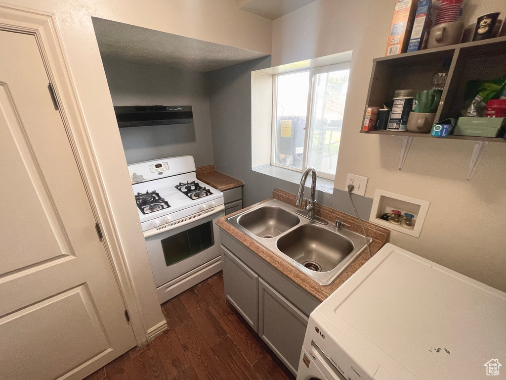 Kitchen with white gas range oven, washer / dryer, dark wood-style floors, and under cabinet range hood
