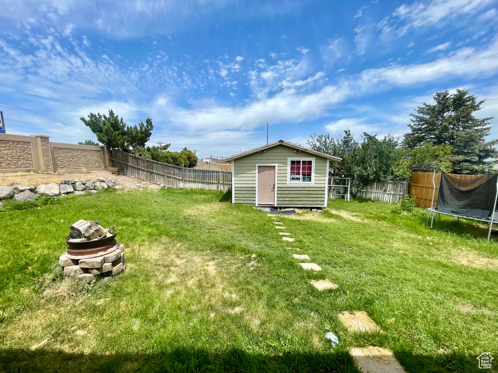 Fenced backyard featuring a trampoline and an outdoor structure
