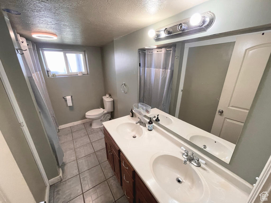 Full bath featuring curtained shower, a textured ceiling, and double vanity