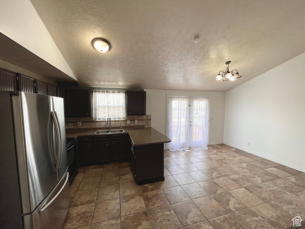 Kitchen featuring freestanding refrigerator, a peninsula, vaulted ceiling, tasteful backsplash, and a chandelier