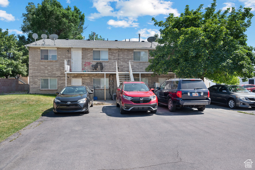 Townhome / multi-family property featuring brick siding, uncovered parking, a front lawn, and a balcony