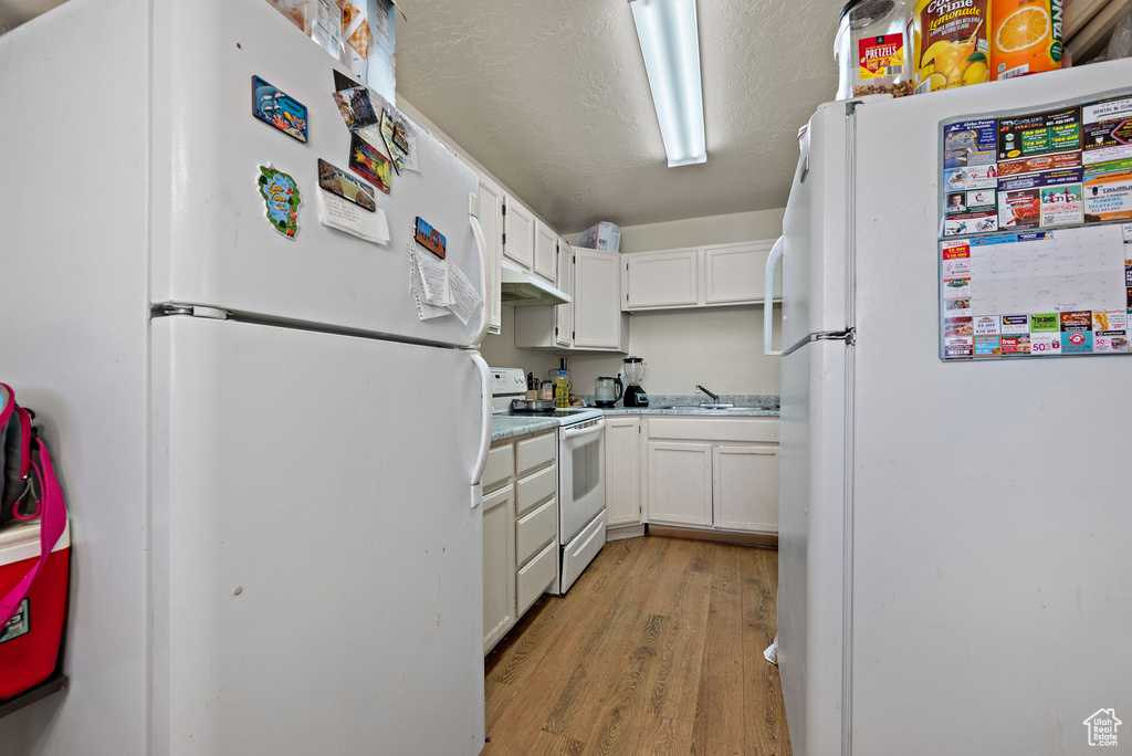 Kitchen featuring white appliances, light wood finished floors, white cabinetry, and light countertops