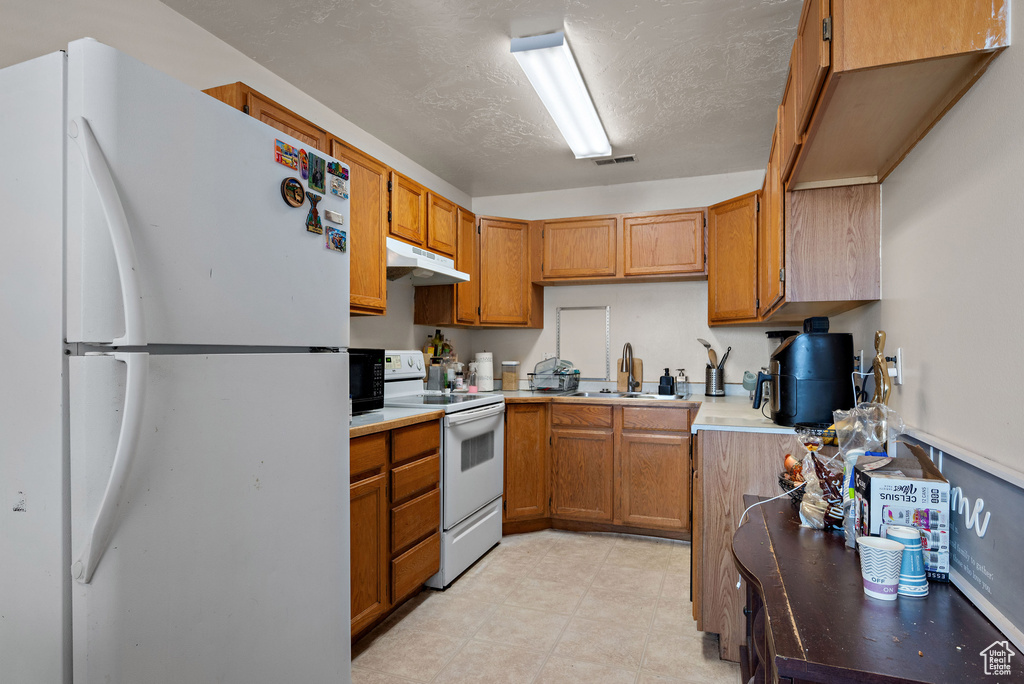Kitchen featuring white appliances, under cabinet range hood, brown cabinetry, and light countertops