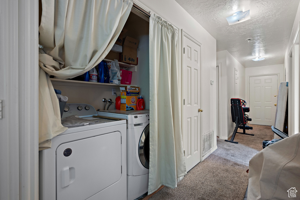 Laundry area featuring washing machine and dryer, carpet, and a textured ceiling